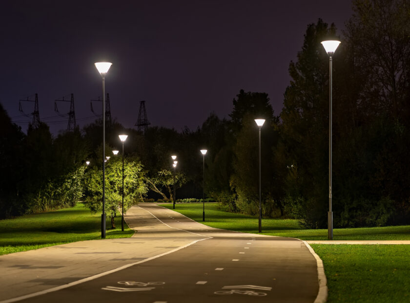 Cycle path in the night park. Lanterns illuminate the lawn, promenade and cycle path surrounded by trees.